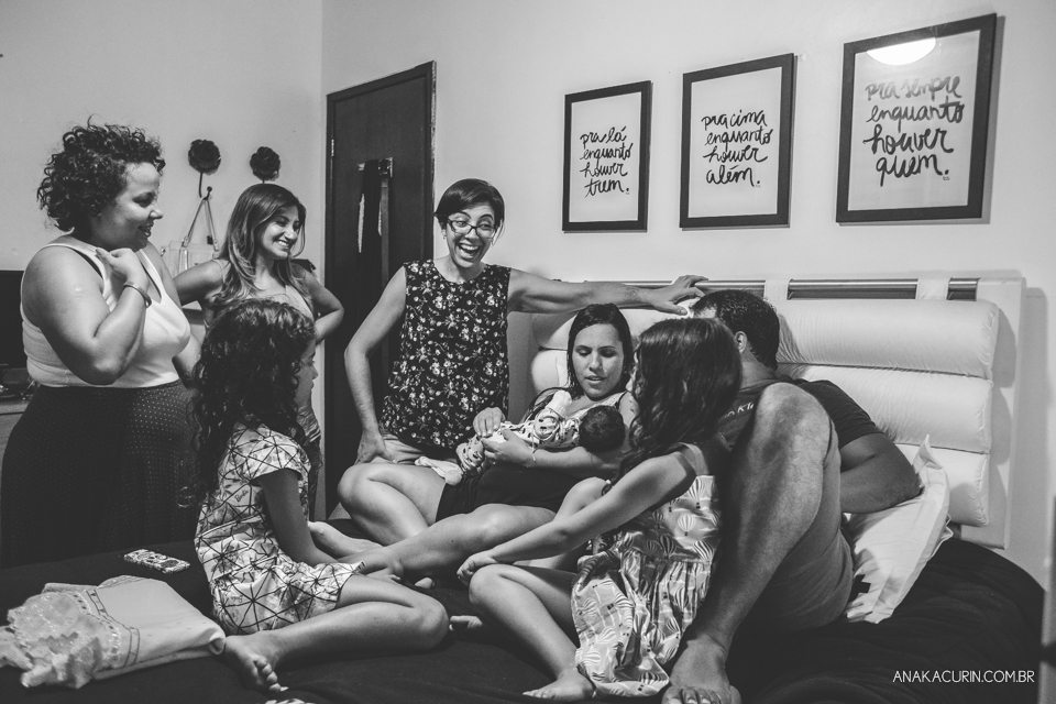 Equipe reunida em volta de mulher recém parida com filho no colo na cama do casal.