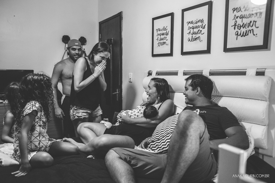 Família reunida em volta de mulher recém parida com filho no colo na cama do casal.