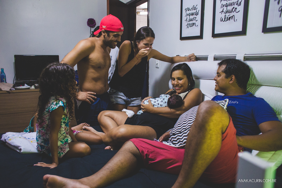 Família reunida em volta de mulher recém parida com filho no colo na cama do casal.