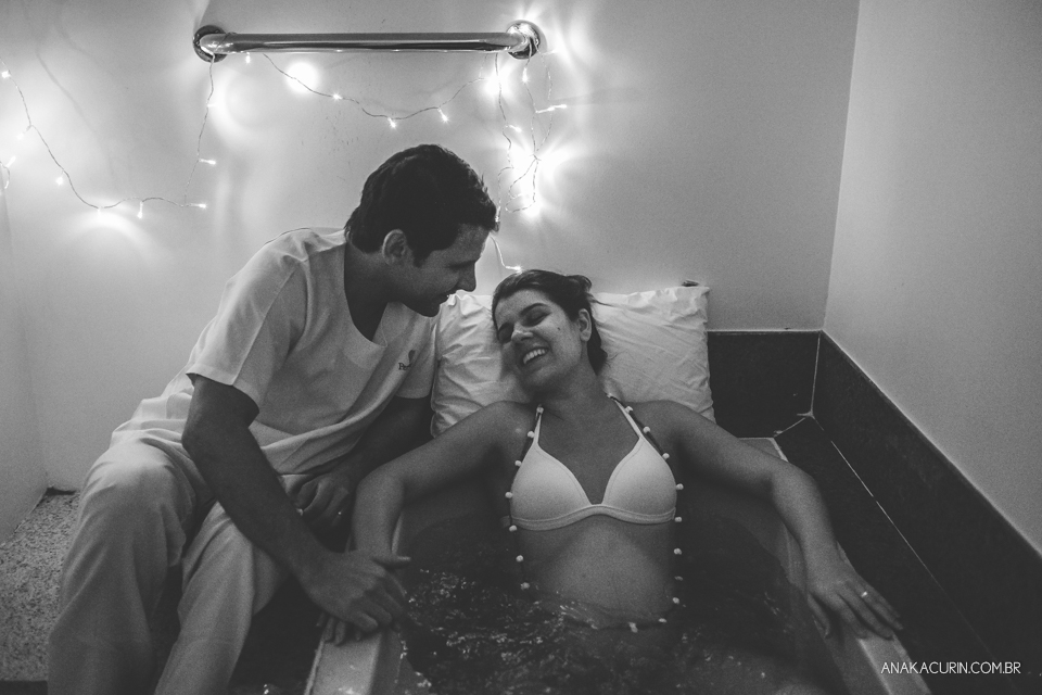 Parto natural hospitalar de Sofia, que aconteceu na Perinatal de Laranjeiras e teve a fotografia feita por Ana Kacurin. Gestante na banheira sorrindo para o pai.