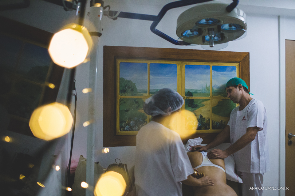 Parto natural hospitalar de Sofia, que aconteceu na Perinatal de Laranjeiras e teve a fotografia feita por Ana Kacurin. Bokeh no primeiro plano, gestante com apoio d doula e pai ao fundo.