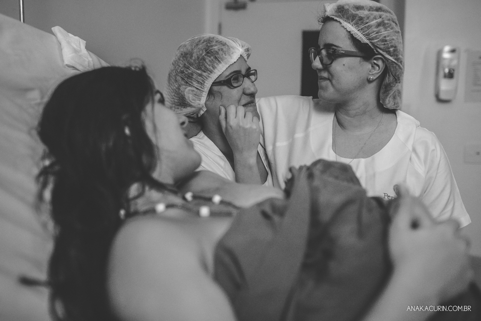 Parto natural hospitalar de Sofia, que aconteceu na Perinatal de Laranjeiras e teve a fotografia feita por Ana Kacurin. Médica e doula se abraçam olhando gestante e bebê.