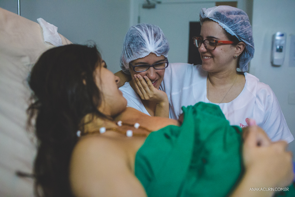 Parto natural hospitalar de Sofia, que aconteceu na Perinatal de Laranjeiras e teve a fotografia feita por Ana Kacurin. Médica e doula se abraçam olhando gestante e bebê.