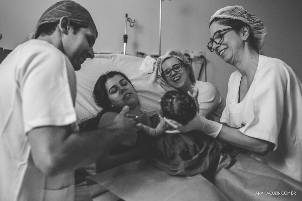 Parto natural hospitalar de Sofia, que aconteceu na Perinatal de Laranjeiras e teve a fotografia feita por Ana Kacurin. Equipe e pais olhando o bebê e sorrindo