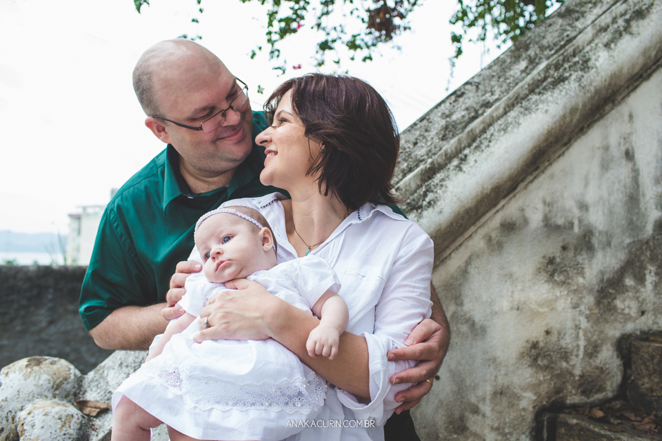 Batizado da Gabi, que aconteceu na igraja Nossa Senhora do Outeiro da Glória, no Rio de Janeiro. Pais se olham com bebê no colo.