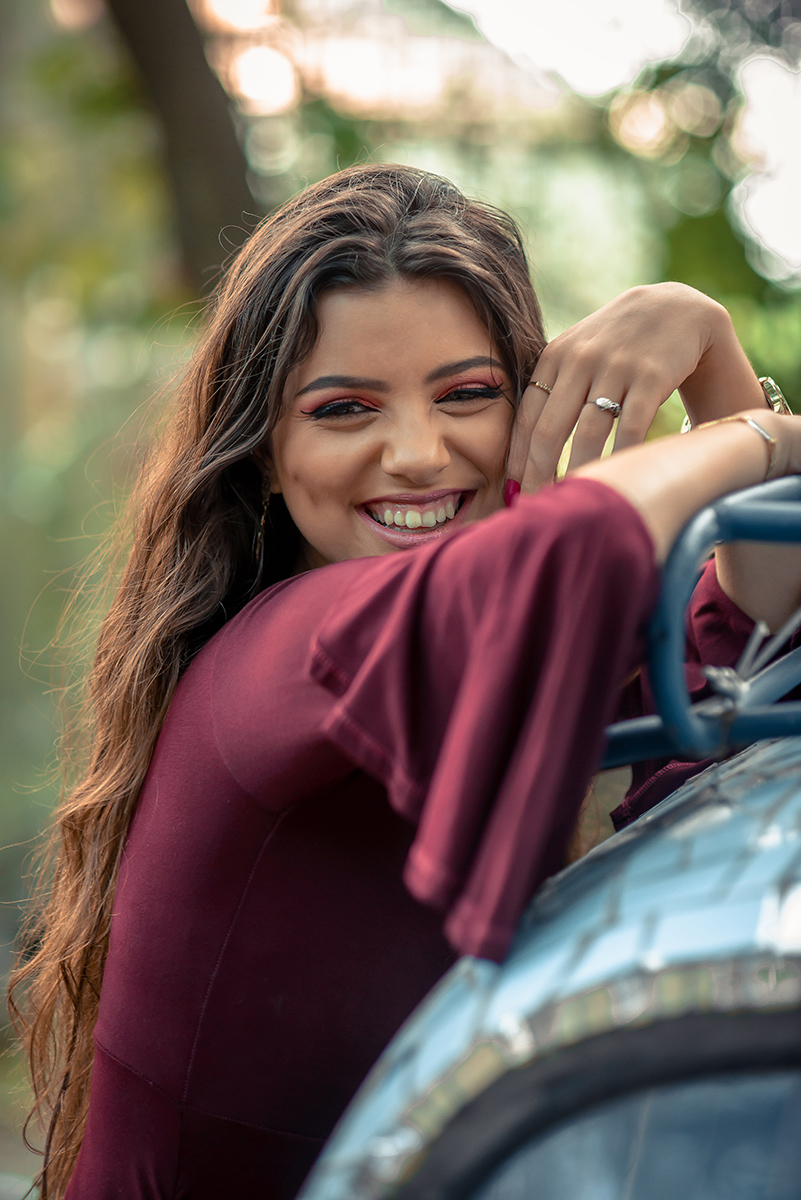 Retrato da linda modelo de olhos verdes com um sorriso lindo usando um vestido vermelho encostada em um fusca durante seu ensaio fotográfico. Foto por Marco Moscarelli Fotógrafo.