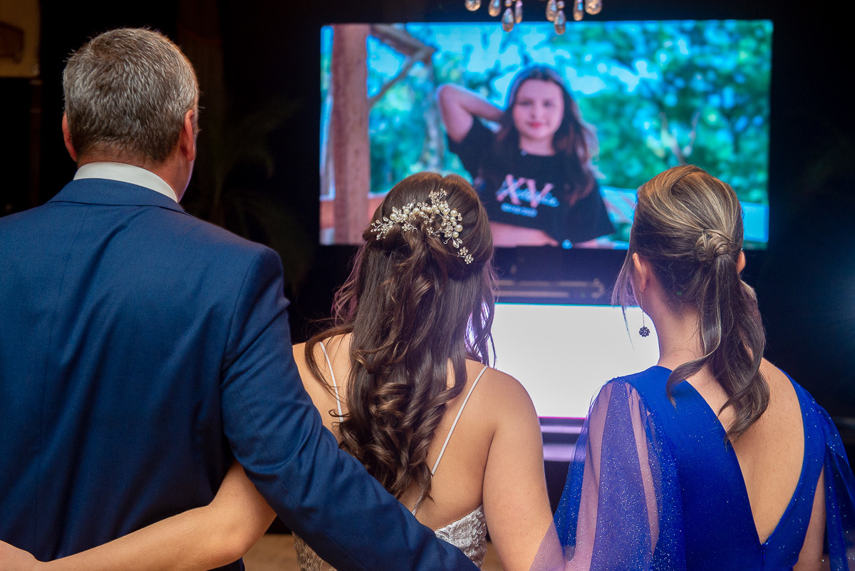 Aniversariante debutante assistindo vídeo de homenagem durante a sua festa de 15 anos. Foto por Marco Moscarelli Fotógrafo Pelotas.