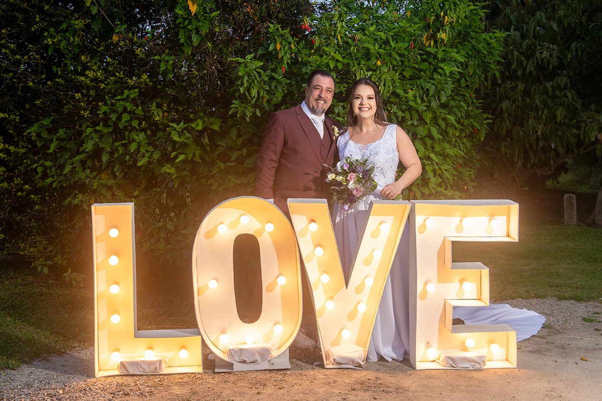Noivos posando em decoração de casamento escrito love após cerimônia de casamento em Pelotas. Foto por Marco Moscarelli Fotógrafo.