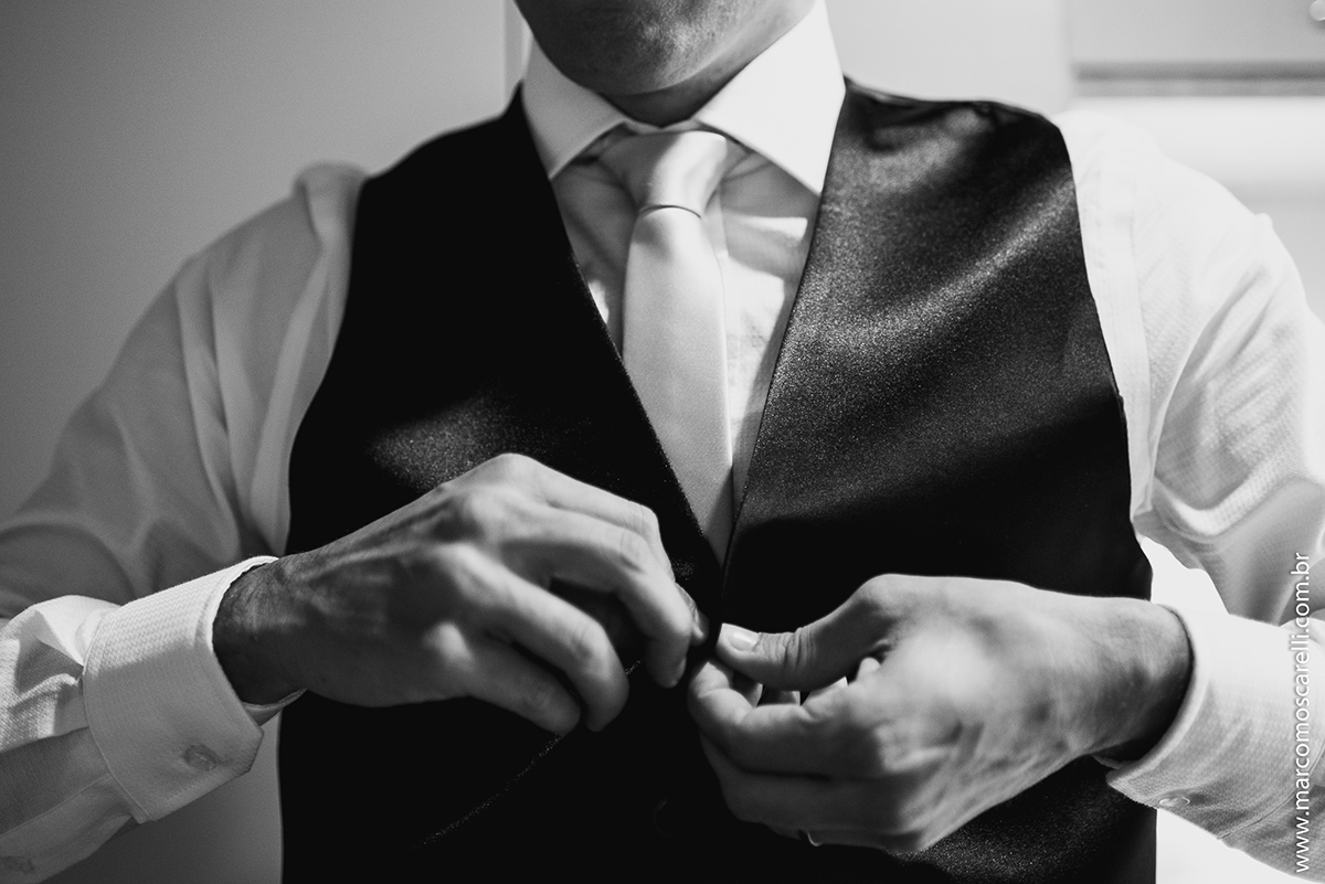 Foto do detalhe do noivo abotoando o colete durante Making of antes do casamento. Foto por Marco Moscarelli