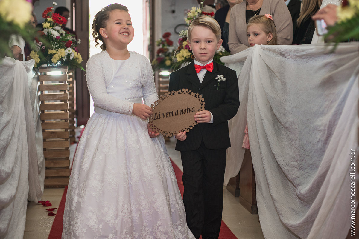 Entrada do pagem e da aia segurando plaquinha de maderia que diz lá vem a noiva durante o casamento. Foto por Marco Moscarelli