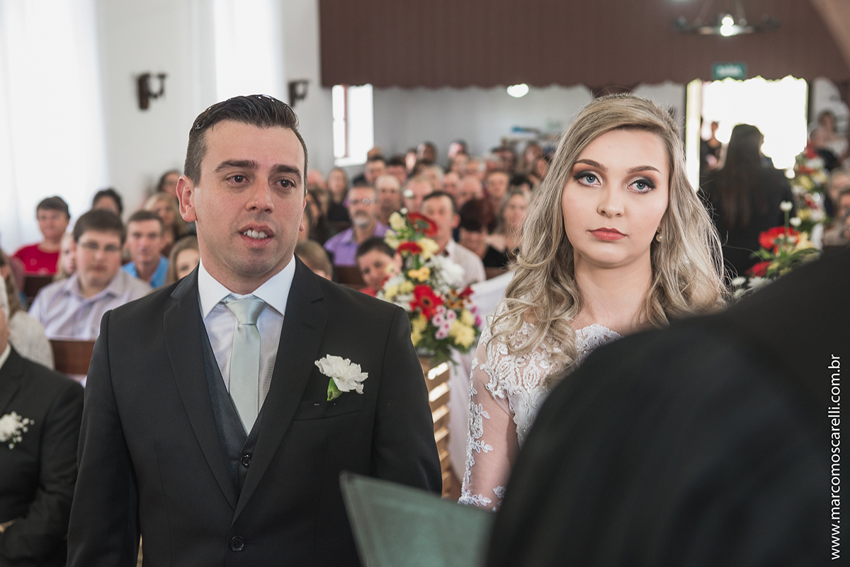 Foto do casal de noivos no altar com a nave da igreja de fundo. Foto por Marco Moscarelli