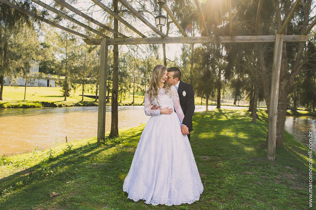 Ensaio dos noivos pós casamento, foto dos noivos ewmldurados por pegolado de maderia com o sol iluminando o vestido da noiva e formando uma bela imagem. Foto por Marco Moscarelli