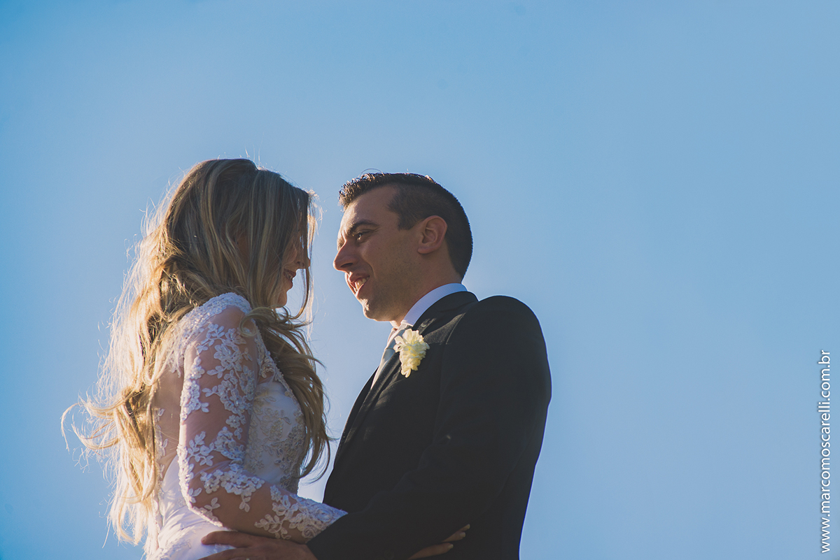Foto contra a luzo do casael de noivos trocando olhares apaixonados com um lindo céu azul de fundo durante ensaio fotográfio após o casamento. Foto por Marco Moscarelli