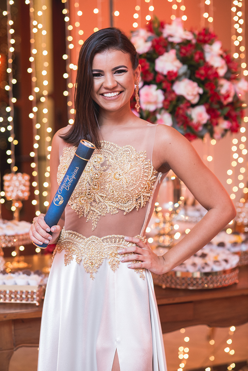 Formanda posando para retrato com seu canudo de formatura em sua recepção de formatura. Marco Moscarelli.