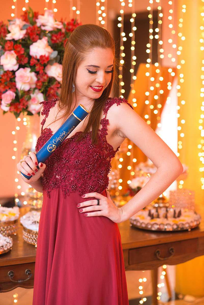 Formanda posando para retrato com seu canudo de formatura em sua recepção de formatura. Marco Moscarelli.