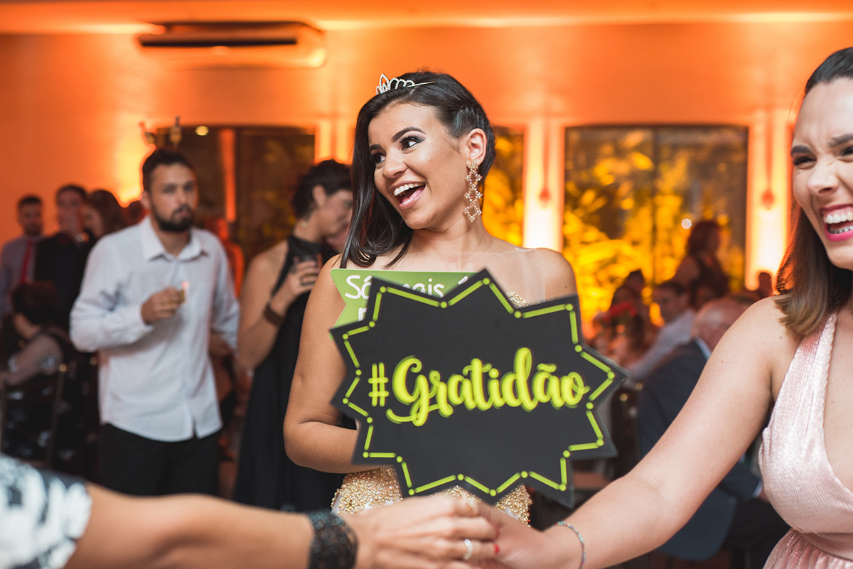 Fotografia da formanda dando um belo sorriso com uma plaquinha divertida escrito gratidão. Foto por Marco Moscarelli.