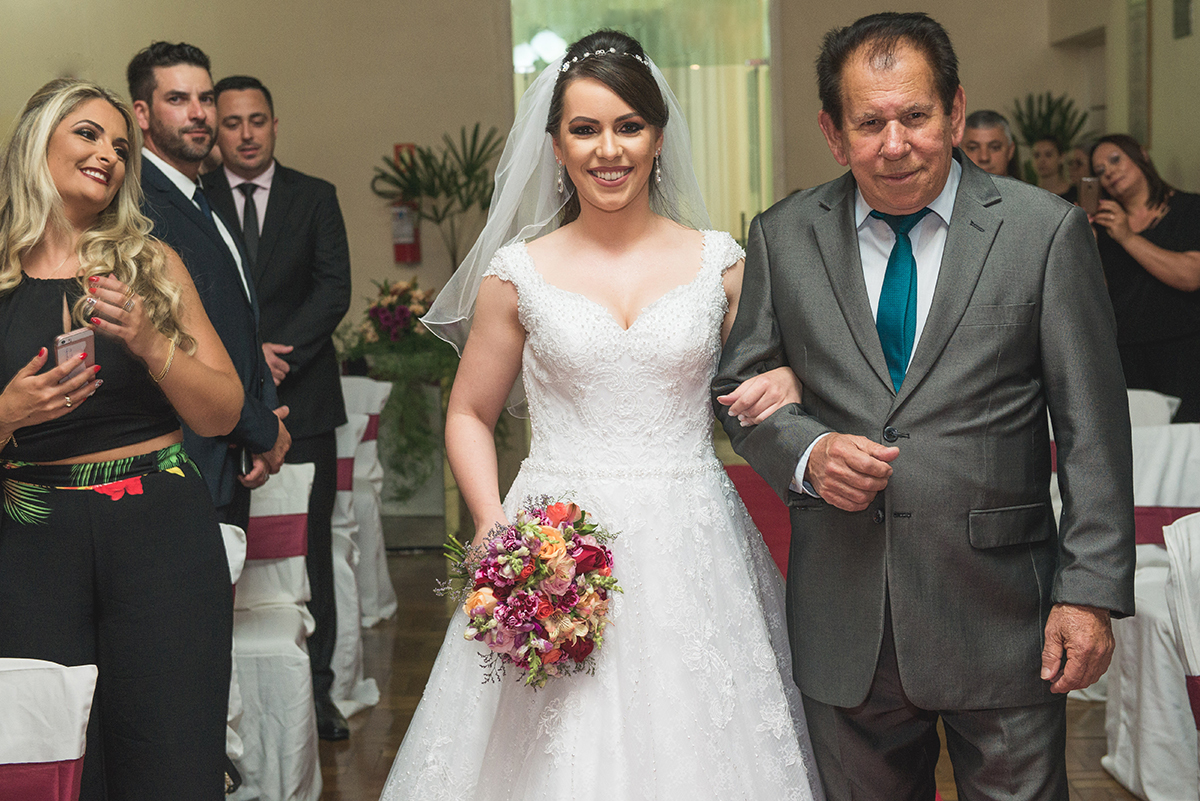 Noiva com um lindo sorriso entrando na cerimônia de casamento acompanhada pelo pai. Foto por Marco Moscarelli Fotografo