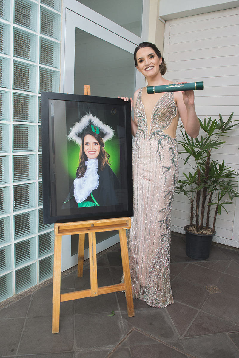 Formanda de medicina posando junto ao seu quadro de formatura. Foto por Marco Moscarelli