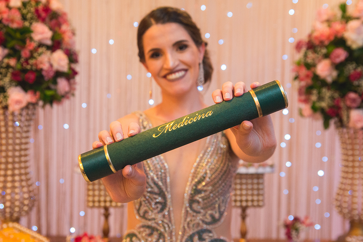 Formanda de medicina posando junto ao seu quadro de formatura. Foto por Marco Moscarelli