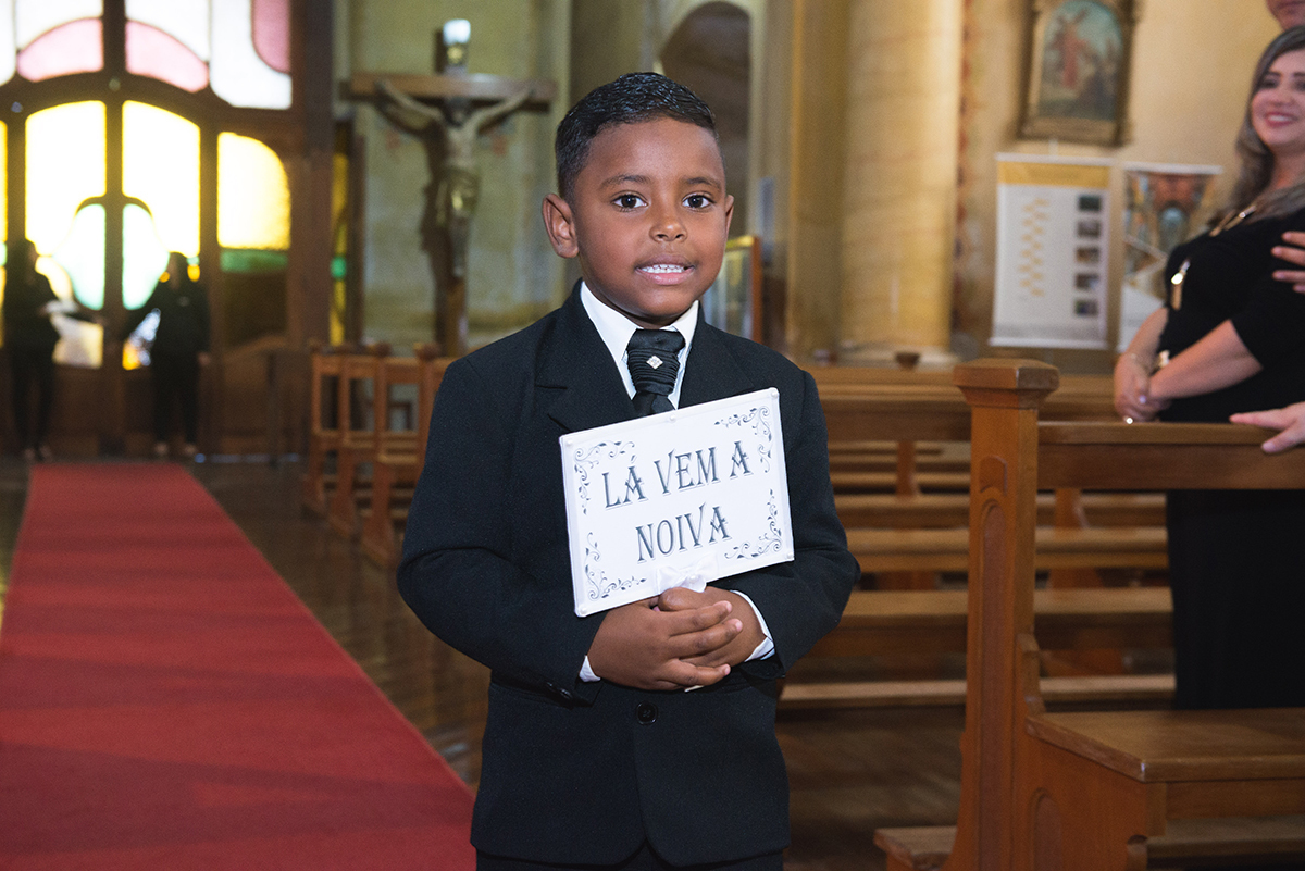Pagem entrando na igreja carregando a plaquinha de la vem a noiva. Foto por Marco Moscarelli