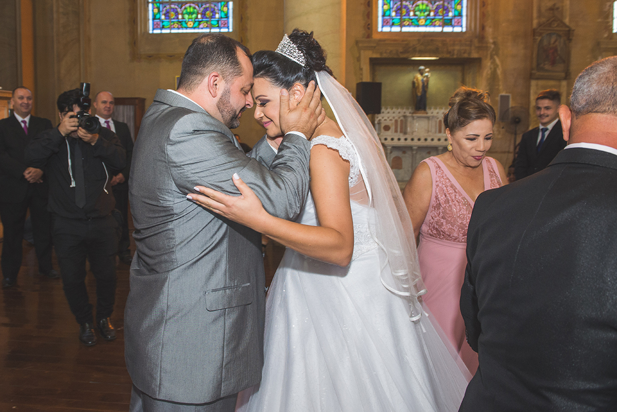 Noivo beijando a noiva na testa no momento em ue a noiva chega ao altar da igreja no dia do casamento. Foto por Marco Moscarelli