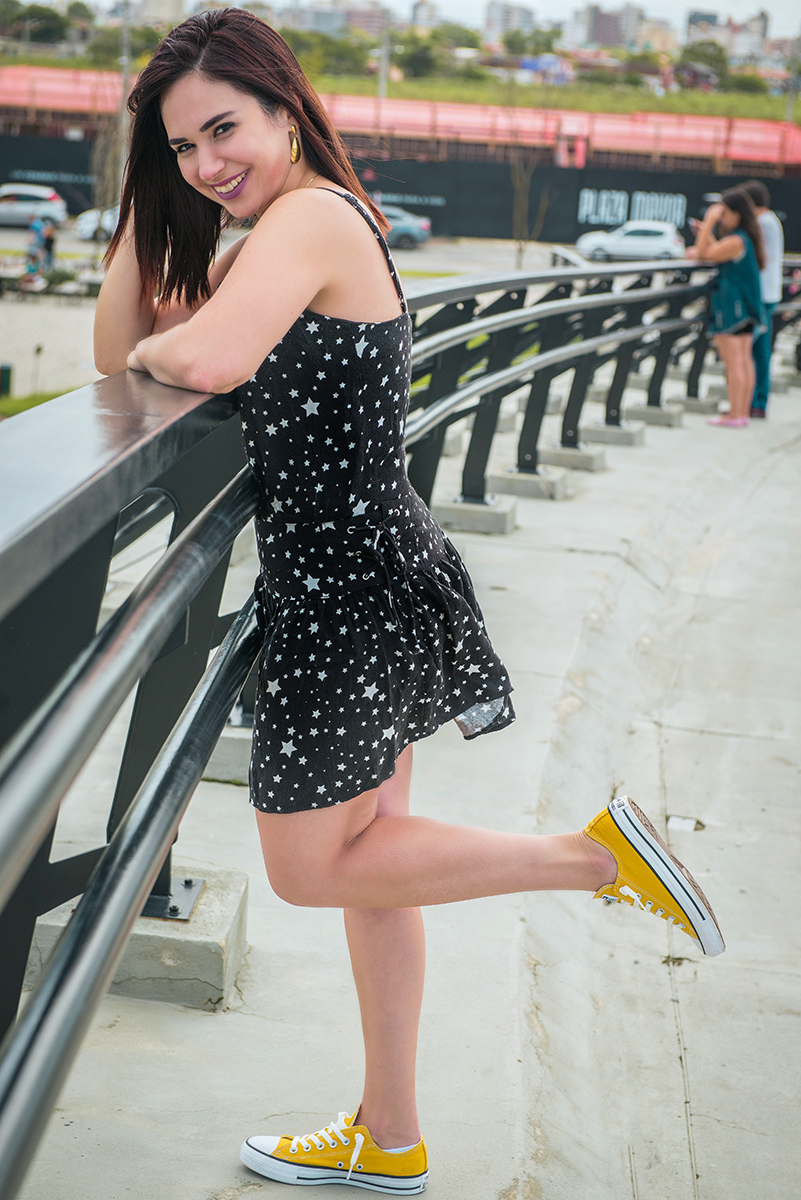 Linda foto da aniversariante no Parque UNa com um vestido preto debruçada em corrimão de passarela sorrindo. Foto por Marco Moscarelli