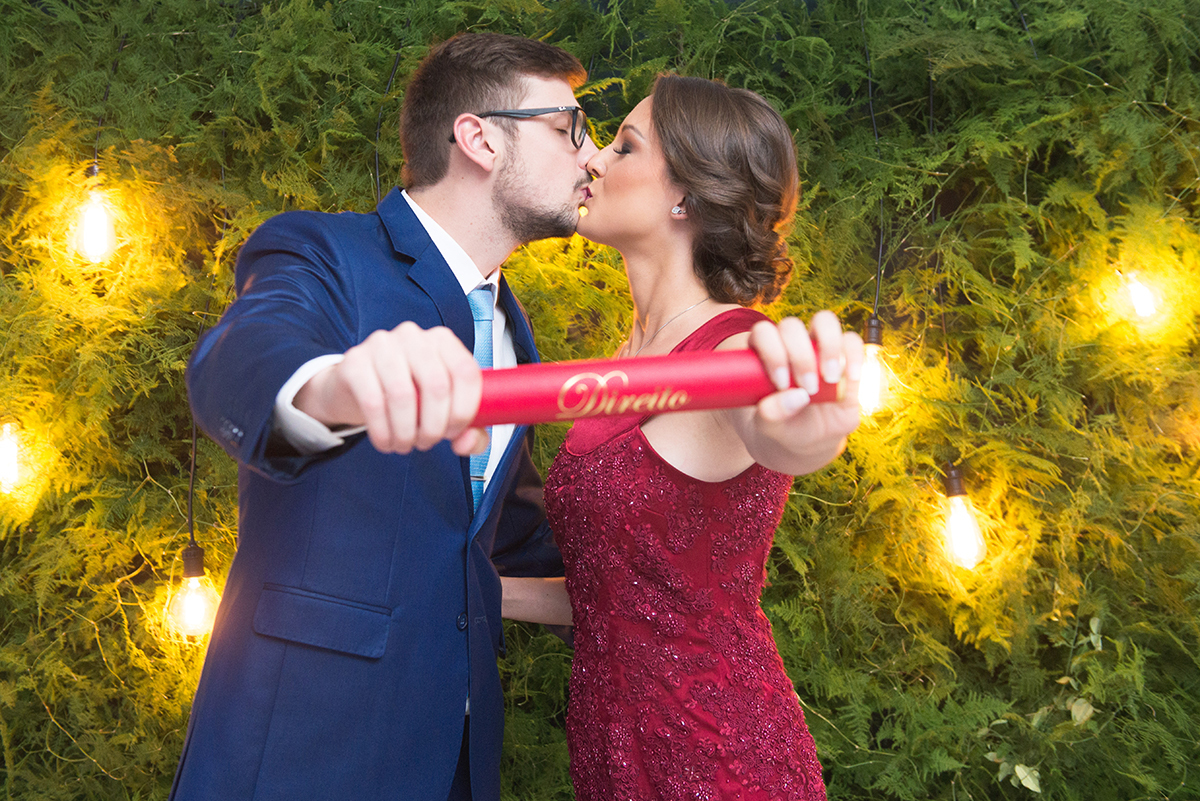 Casal de noivos e formandos posando para fotos no painel com um lindo beijo e  seus respectivos canudos de formatura. Foto por Marco Moscarelli Fotografo.