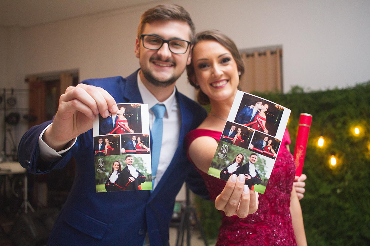 Casal de formandos e noivos posando para fotos com fotos instantâneas usadas como lembrança da recepção de formatura. Foto por Marco Moscarelli Fotografo. 