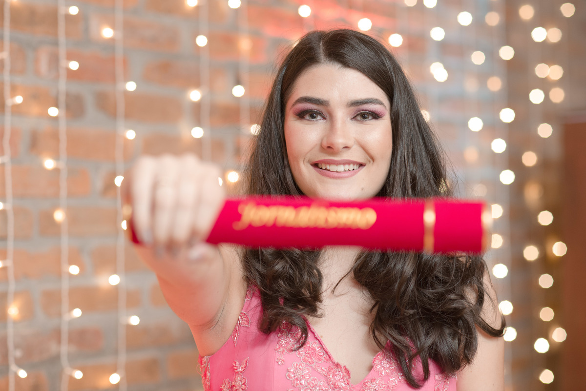 Formanda posando para foto com seu canudo de formatura em jornalismo pela UFPEL. Foto por Marco Moscarelli Fotografo.