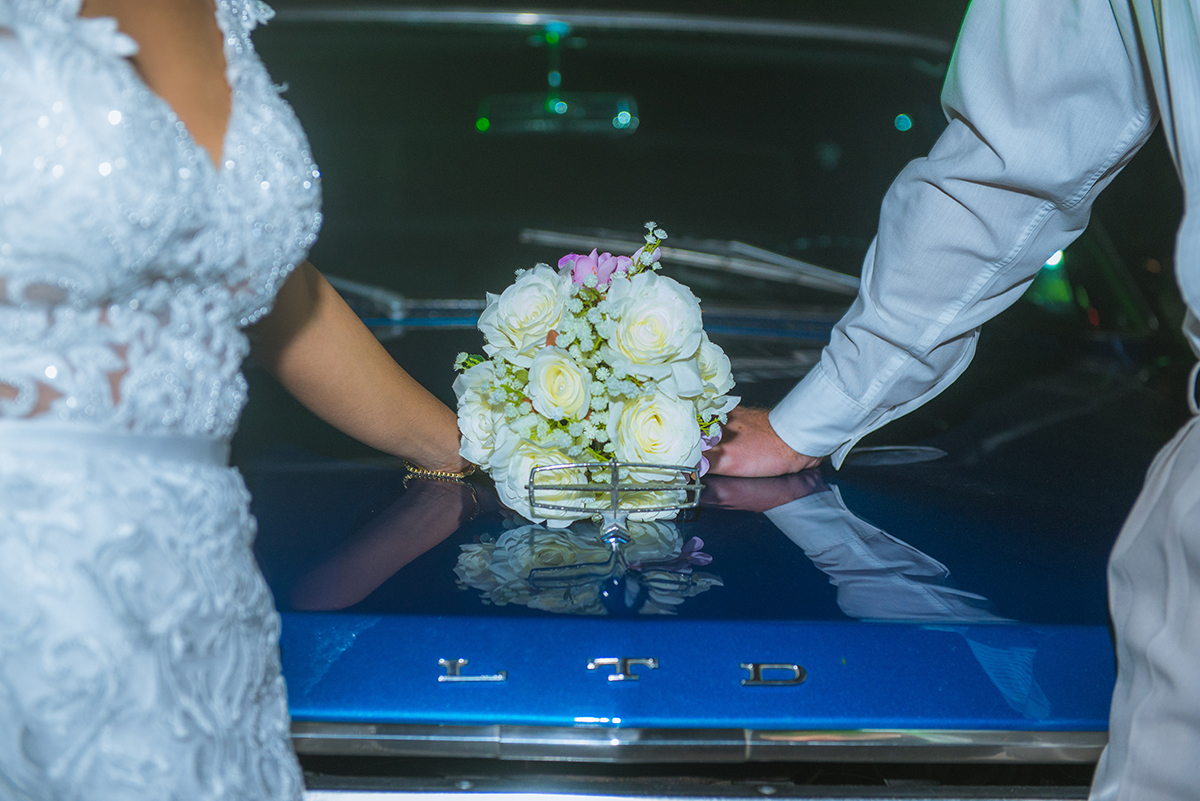 Noivos posando com o buque da noiva no capo do carro da noiva. Foto por Marco Moscarelli