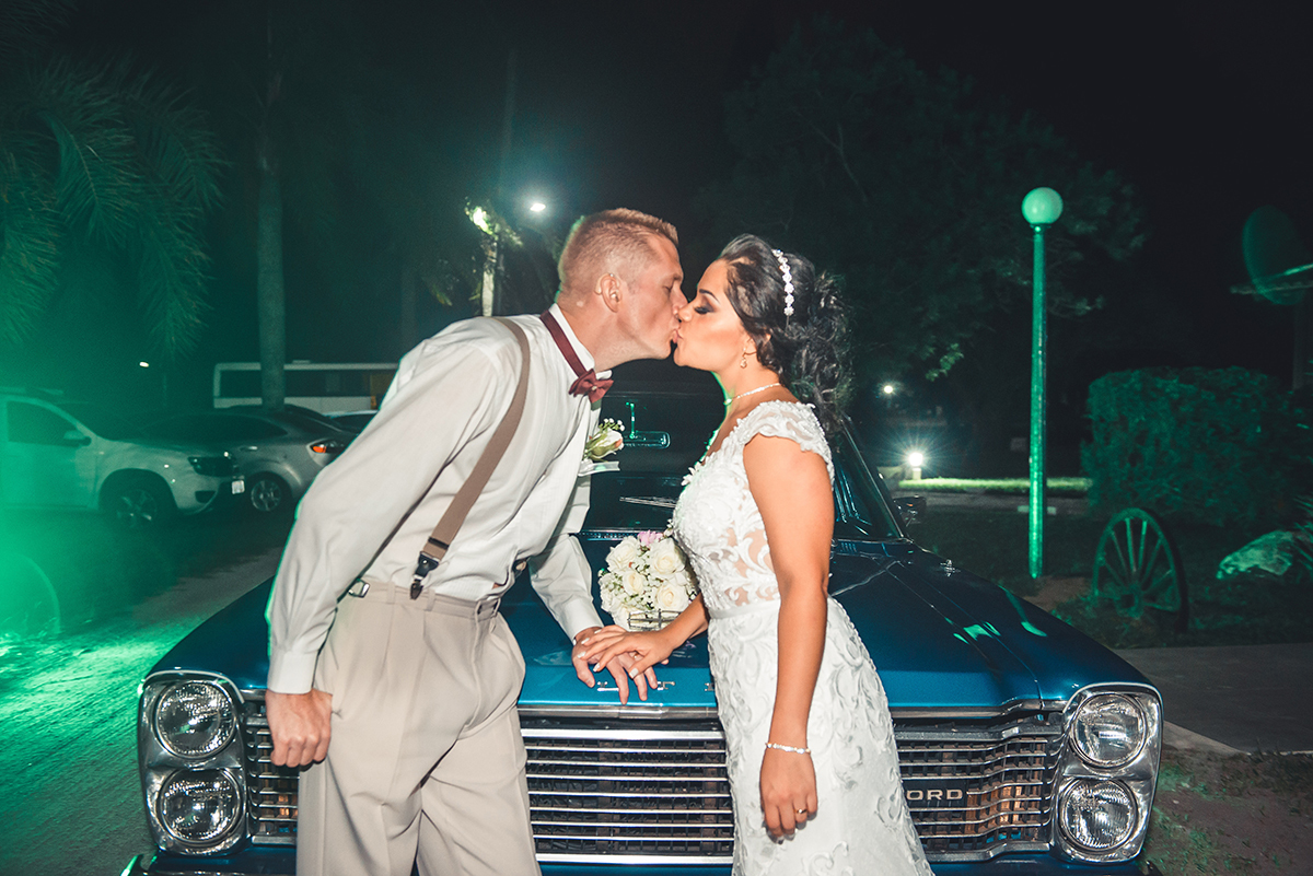 Noivos posando com o buque da noiva e um lindo beijo  no capo do carro da noiva. Foto por Marco Moscarelli