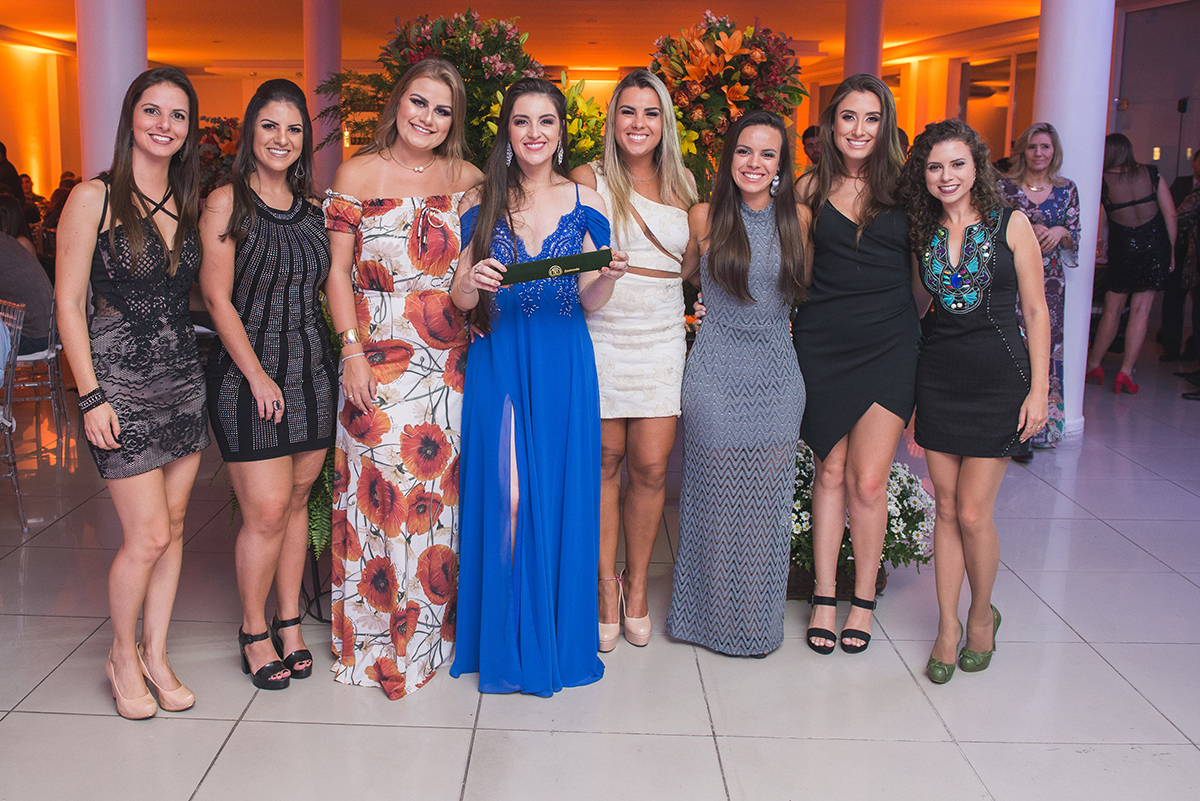 Formanda posando para fotos com suas convidadas e o cartaz de formatura.  Foto por Marco Moscarelli Fotografo