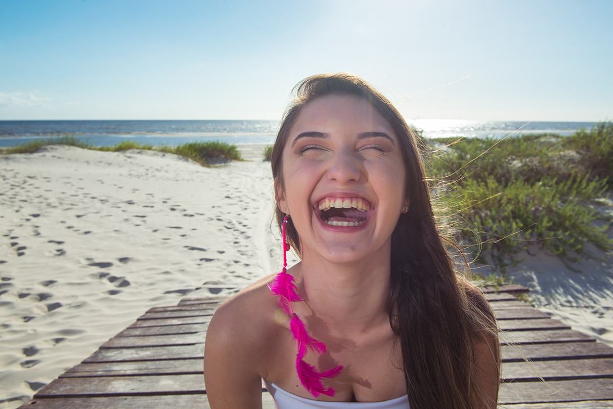 Linda foto da debutante sentada no trapiche  com um lindo sorriso durante seu ensaio de 15 anos na praia da capilha. Foto por Marco Moscarelli Fotografo.