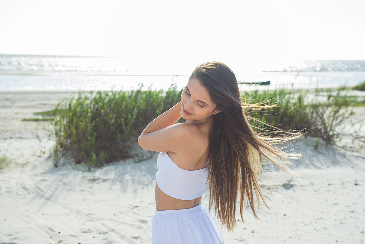 Linda foto da debutante olhando para trás com os cabelos ao vento durante seu ensaio de 15 anos na praia da capilha. Foto por Marco Moscarelli Fotografo.