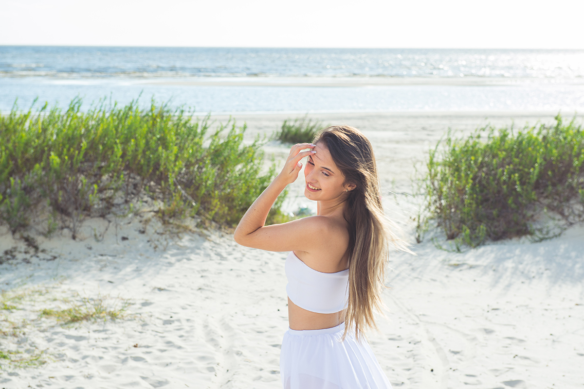 Linda foto da debutante olhando para trás com os cabelos ao vento durante seu ensaio de 15 anos na praia da capilha. Foto por Marco Moscarelli Fotografo.