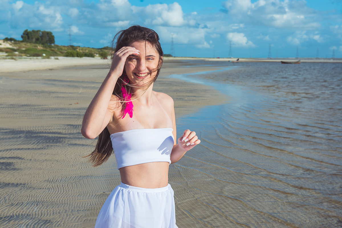 Linda foto da debutante caminhando pela praia com um belo sorriso no rosto durante seu ensaio de 15 anos na praia da capilha. Foto por Marco Moscarelli Fotografo.