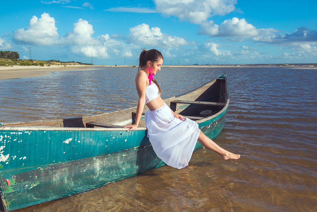 Linda foto da debutante sentada barco brincando com a água  durante seu ensaio de 15 anos na praia da capilha. Foto por Marco Moscarelli Fotografo.