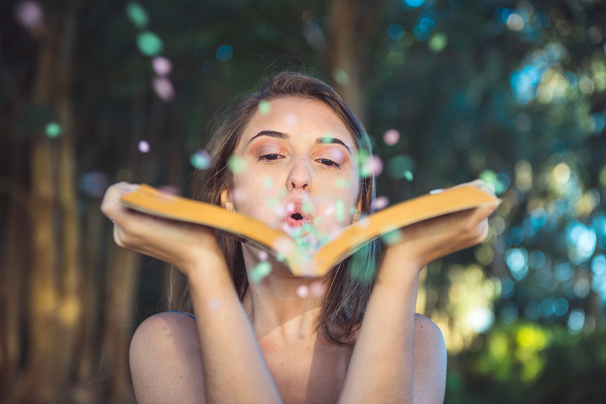 Fotografia da debutante soprando confetes de um livro aberto durante o seu ensaio fotográfico na praia da capilha. Foto por Marco Moscarelli Fotografo.