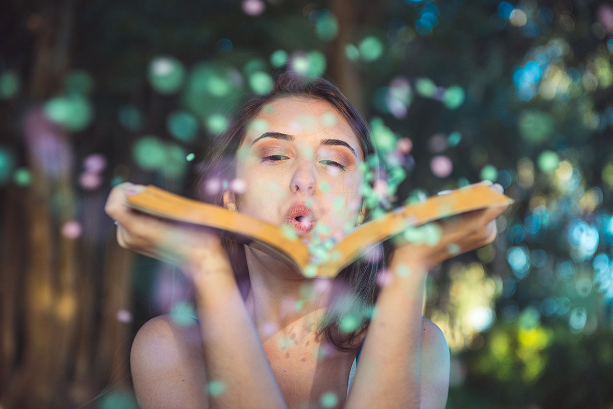 Fotografia da debutante soprando confetes de um livro aberto durante o seu ensaio fotográfico na praia da capilha. Foto por Marco Moscarelli Fotografo.