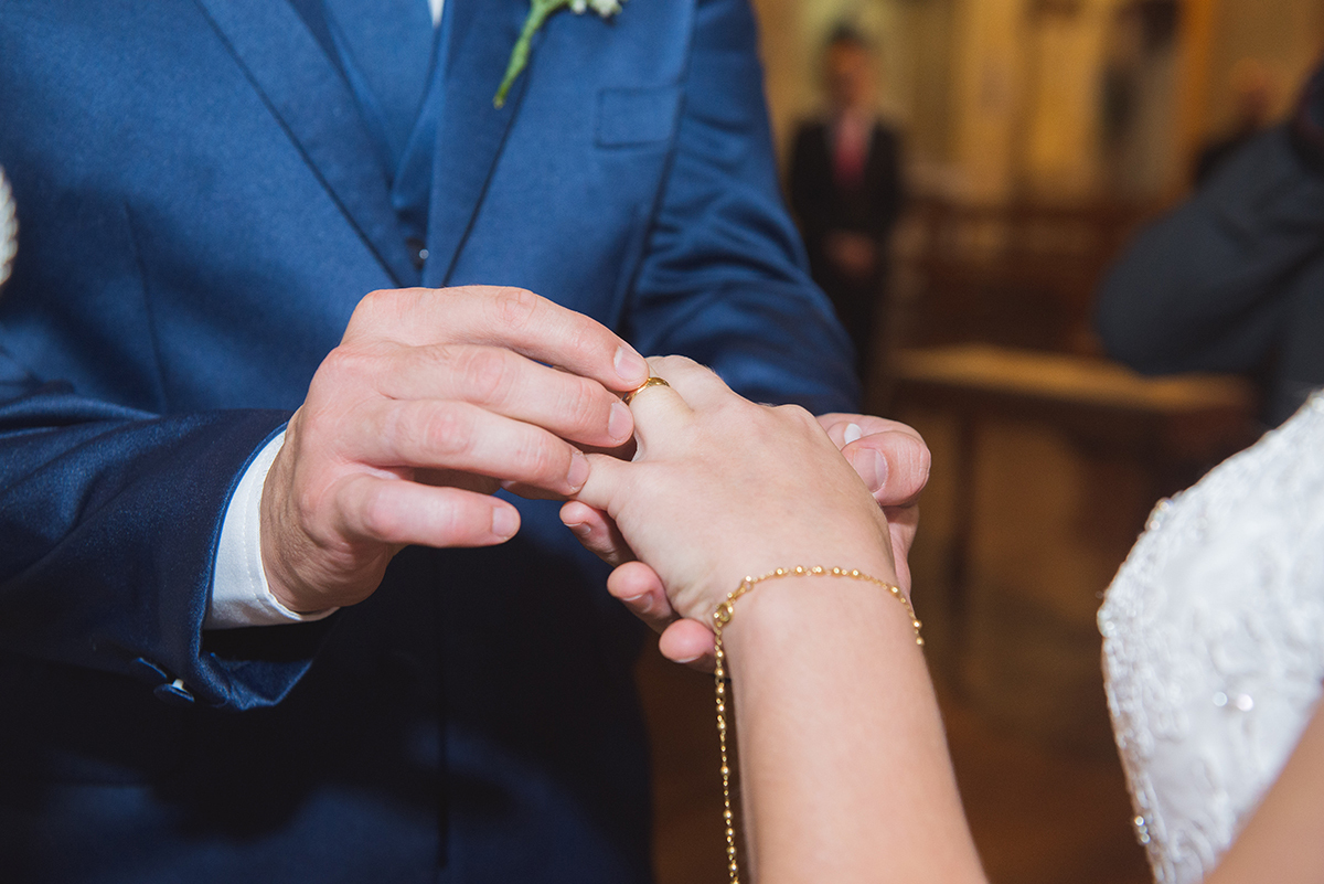Detalhe do noivo colocando a aliança no dedo da noiva durante a cerimônia de casamento.