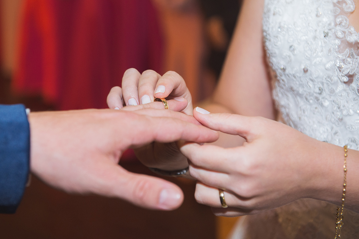 Detalhe do noivo colocando a aliança no dedo da noiva durante a cerimônia de casamento.