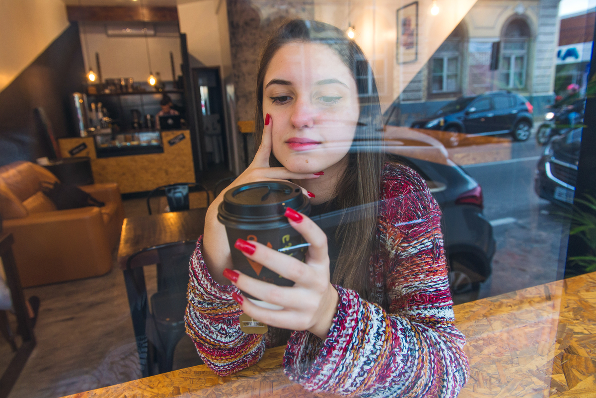 Foto descontraida da debutante através da janela de um café durante o seu ensaio fotográfico de 15 anos. Foto por Marco Moscarelli Fotografo.