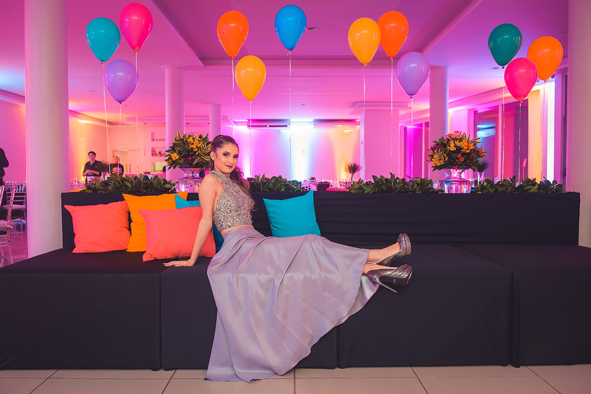 Aniversariante posando para fotos sentada em lindo sofá que compõe a decoração da festa de 15 anos. Foto por Marco Moscarelli Fotografo.