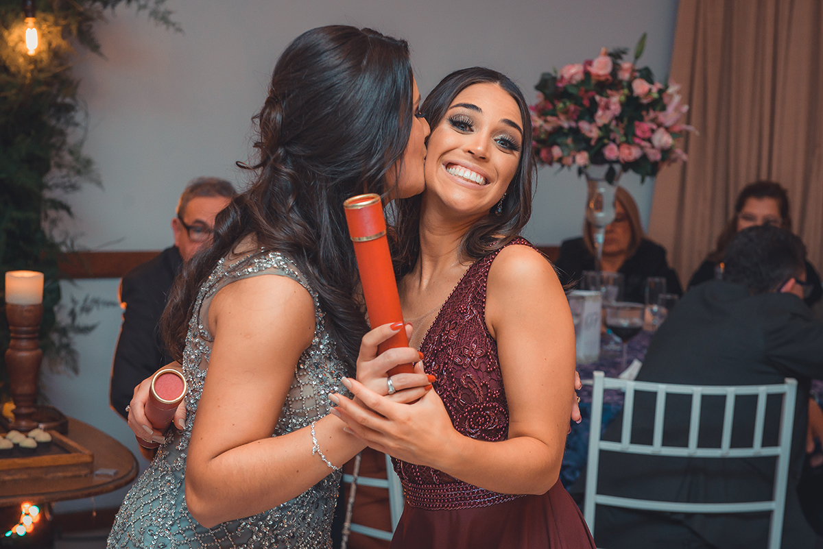 Momento descontraído da formanda dando um beijo em sua colega durante a sua recepção de formatura. Foto por Marco Moscarelli Fotografo.