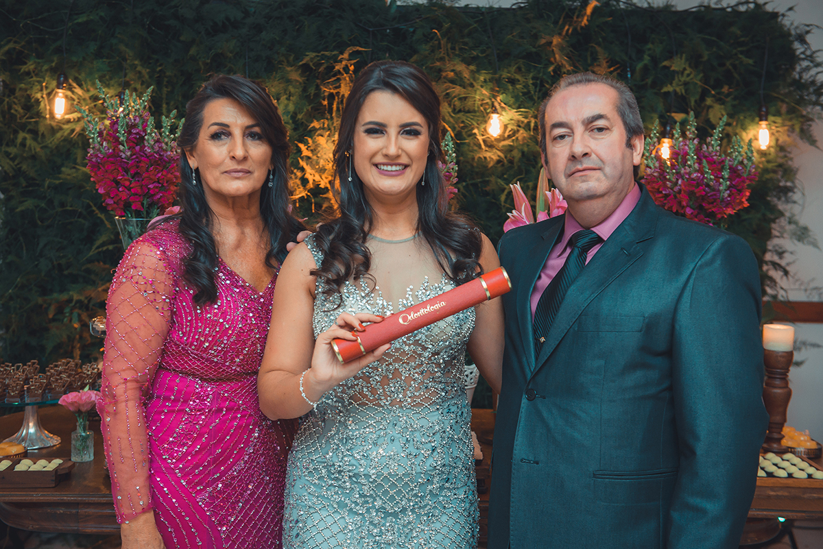 Formanda em odontologia posando para fotos com seus pais e com o canudo de formatura nas mãos. Foto por Marco Moscarelli Fotografo