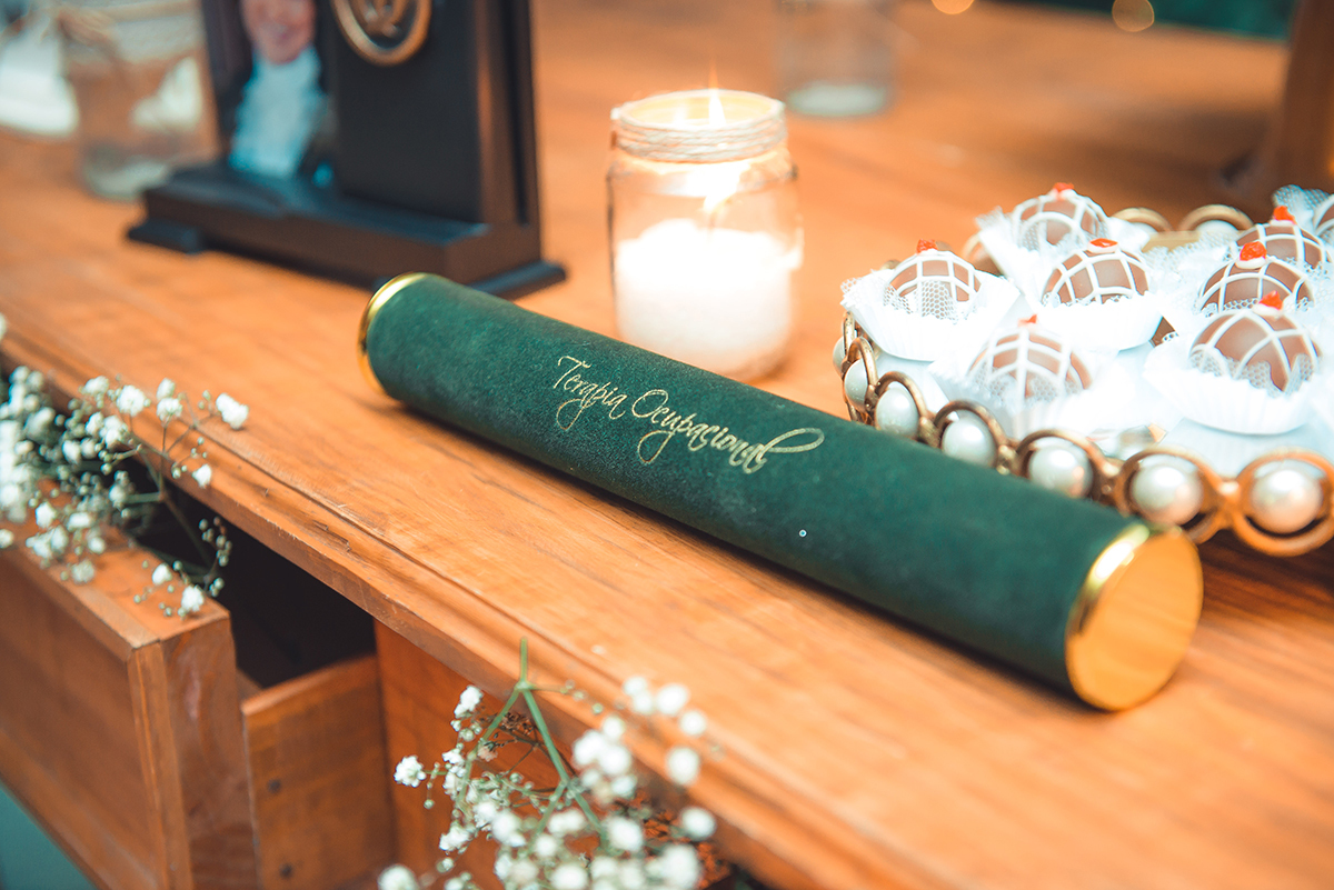 Fotografia do canudo de formatura apoiado sobre a mesa de que compõe a decoração de formatura. Foto por Marco Moscarelli Fotografo.