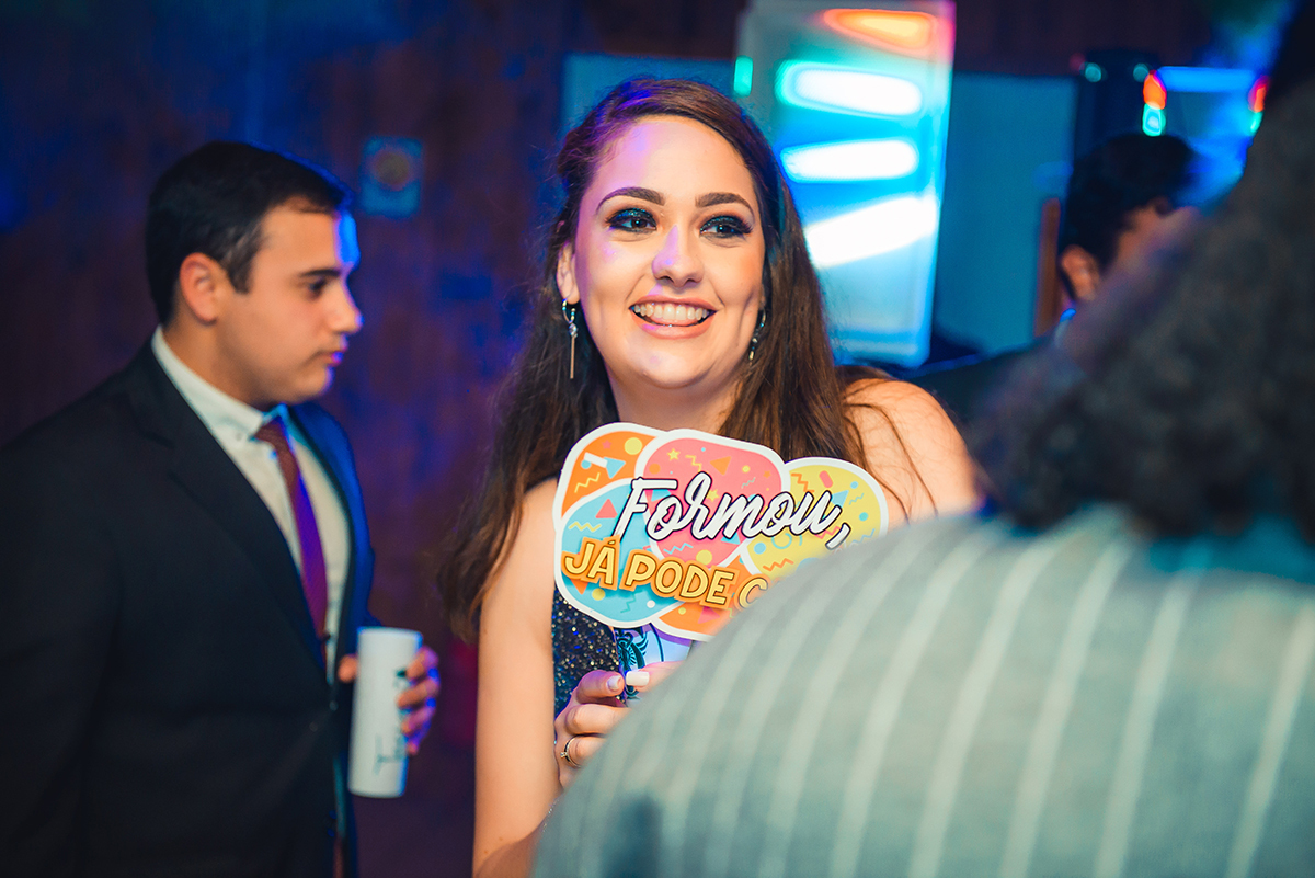 Formanda dançando feliz durante a sua recepção de formatura com cartaz na mão. Foto por Marco Moscarelli Fotografo.