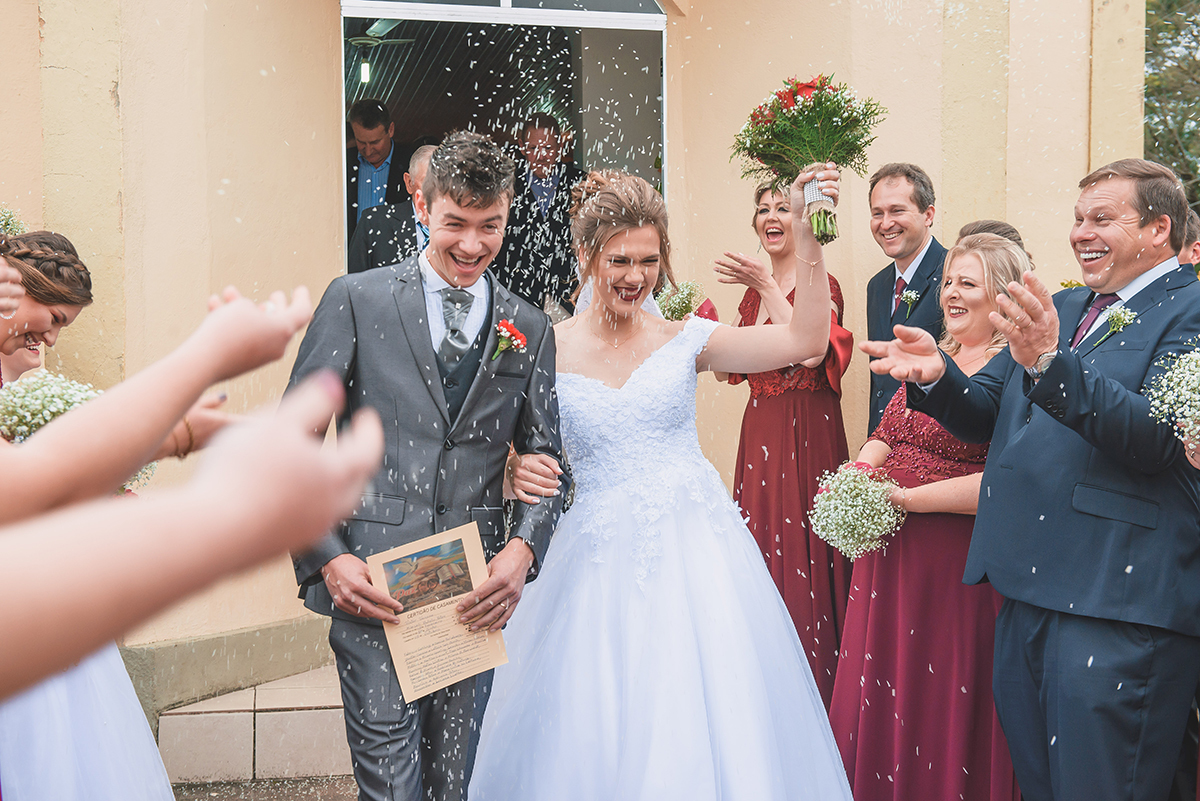 Saída dos noivos da igreja ao final do casamento debaixo de muita chuva de arroz dos padrinhos.  Foto por Marco Moscarelli Fotografo Pelotas.