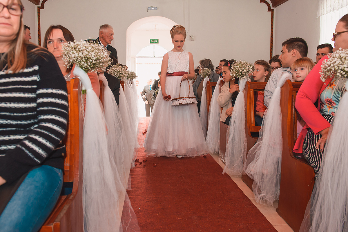 Aia do casamento entrando na igreja derramando pétalas de rosas pelo caminho.Foto por Marco Moscarelli Fotografo Pelotas.