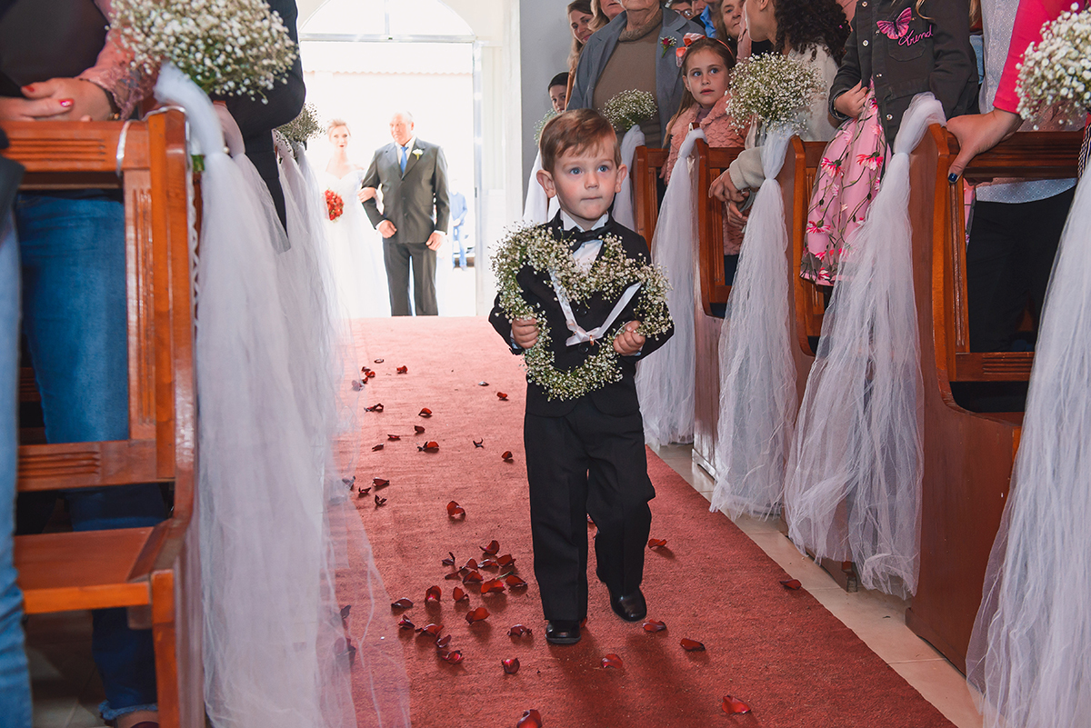 Pagem do casamento entrando na igreja carregando um lindo coração decorado com flores. Foto por Marco Moscarelli Fotografo Pelotas.
